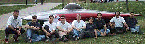 [Team on the grass in front of red car]