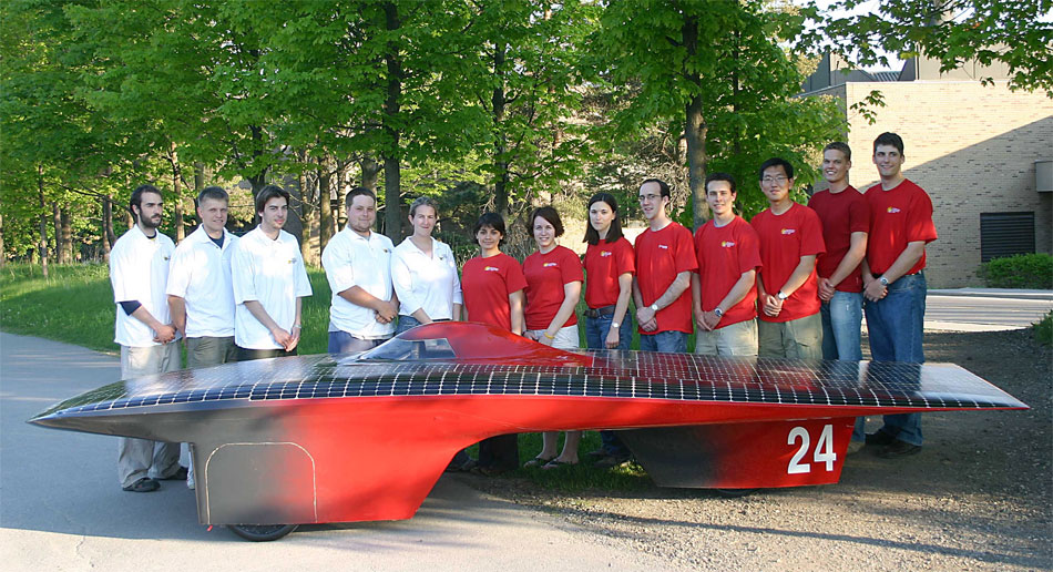 [Student team with solar car and trees]