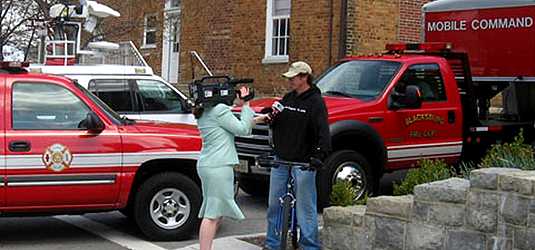 [Reporter with camera interviews student in front of fire trucks]