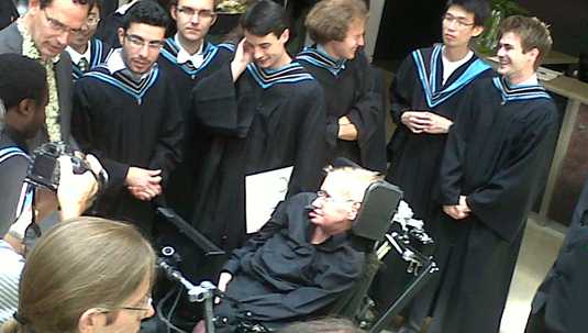 [Hawking in black surrounded by students in black]