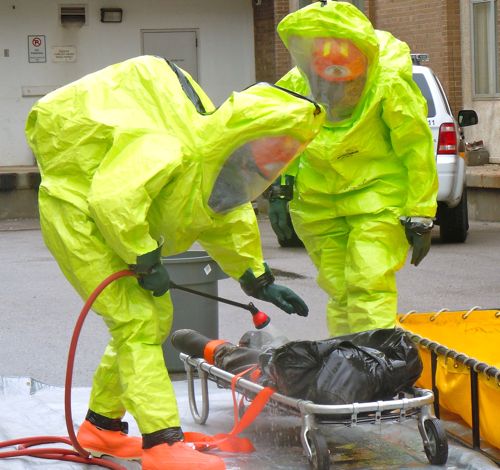Workers in yellow hazmat suits spray a dummy victim with decontaminant