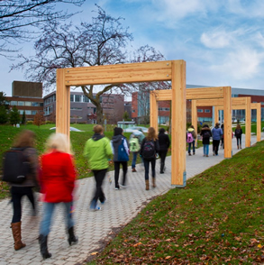 Students walk under the cedar arches at the redesigned campus gateway.