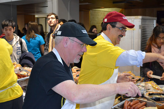 Dean of Arts Douglas Peers and President Feridun Hamdullahpur pass out hot dogs to students in the Student LIfe Centre Great Hall.