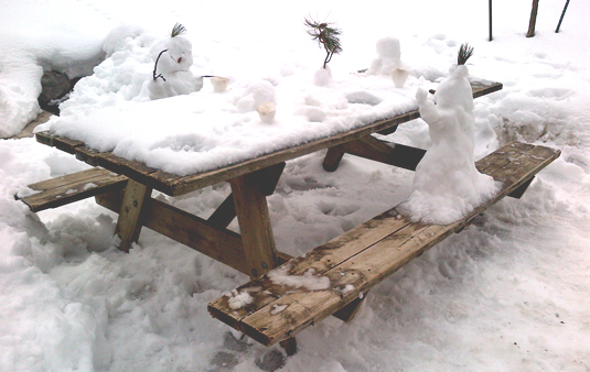 Snowpeople enjoying a frozen drink at a picnic table.