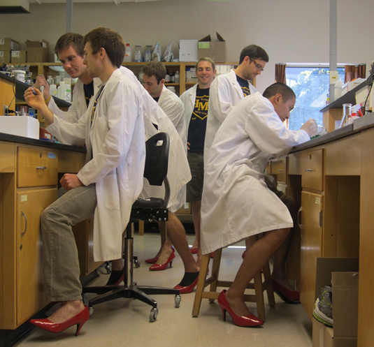 Male students wearing lab coats and red high-heel shoes.