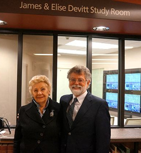 Elise poses with Librarian Mark Haslett in front of the James & Elise Devitt Study Room.