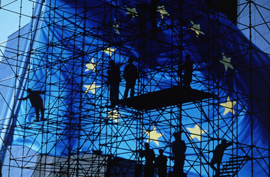 Workers erect a scaffold in front of a large flag of the European Union.