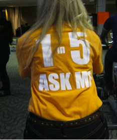 A woman wearing an orange shirt that says "ask me" on the back.