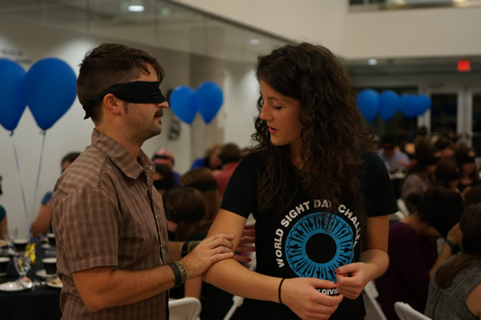 A volunteer leads a blindfolded attendant at the Dining in the Dark event.